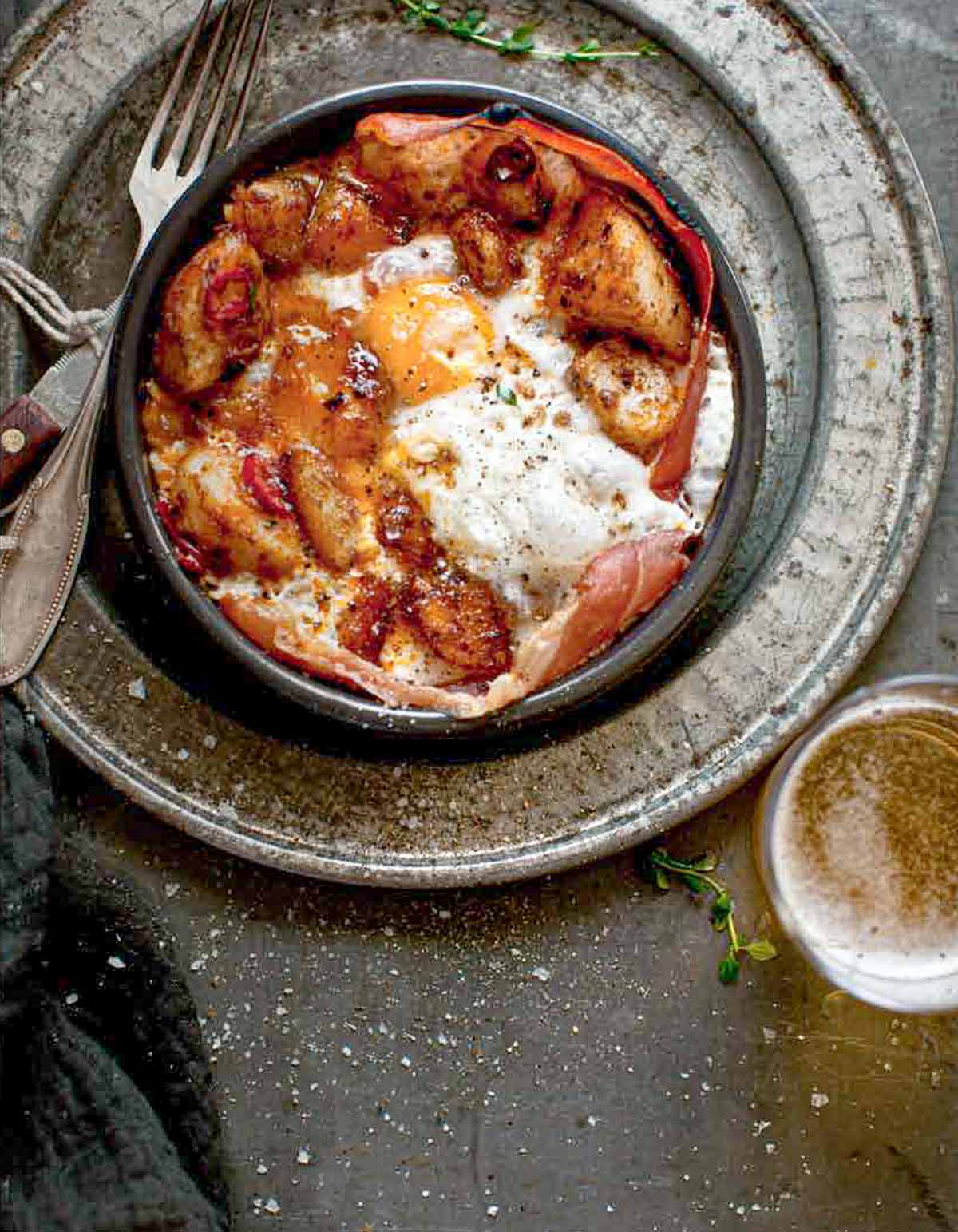 A bowl of patatas bravas with ham and egg - crispy potatoes, ham, and fried egg - with a fork resting beside it.