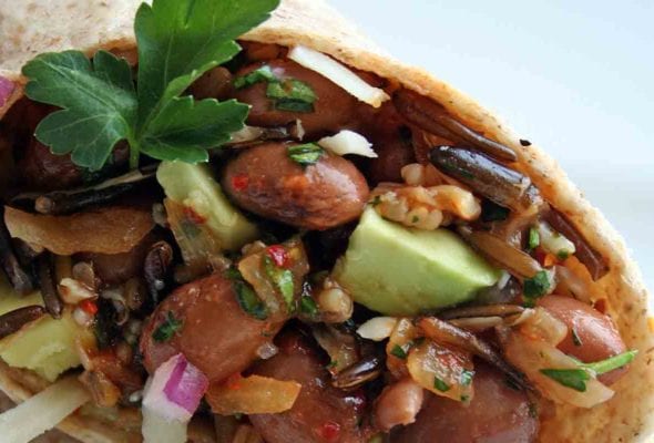 A pinto bean, quinoa, and wild rice wrap, cut in half and garnished with a sprig of parsley.