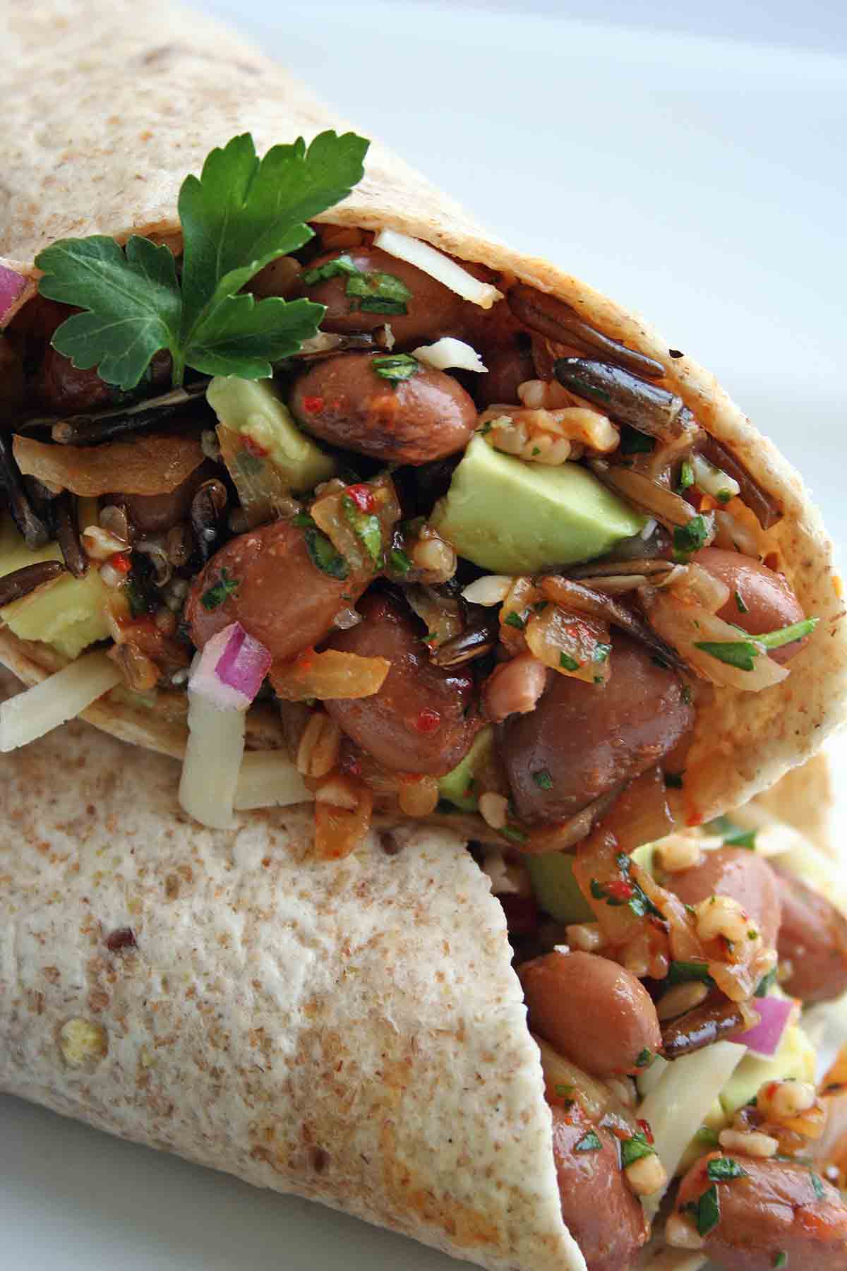 A pinto bean, quinoa, and wild rice wrap, cut in half and garnished with a sprig of parsley.