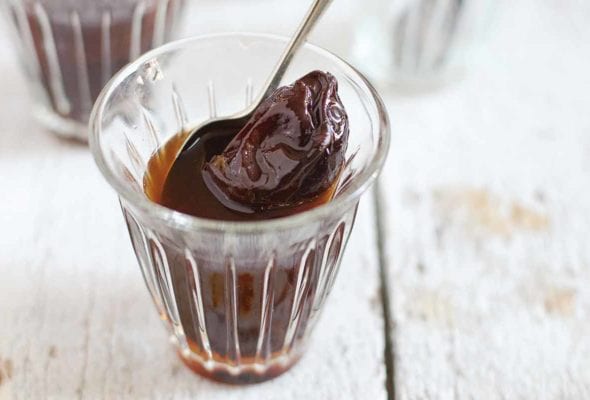 Two small glasses filled with prunes in rum and a spoon resting inside each glass.