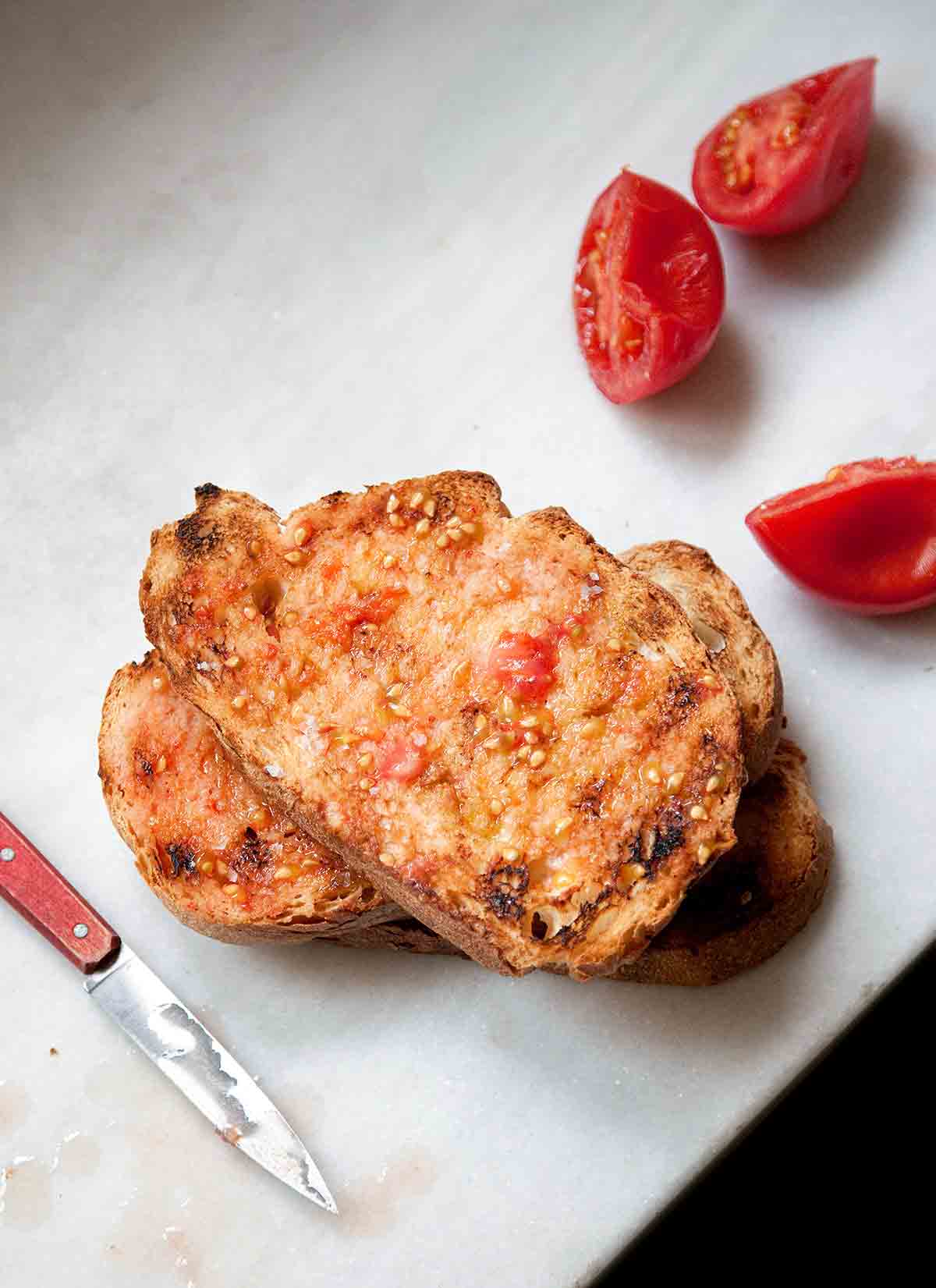 Two slices of tomato rubbed bread and three tomato halves that have been rubbed on the bread.