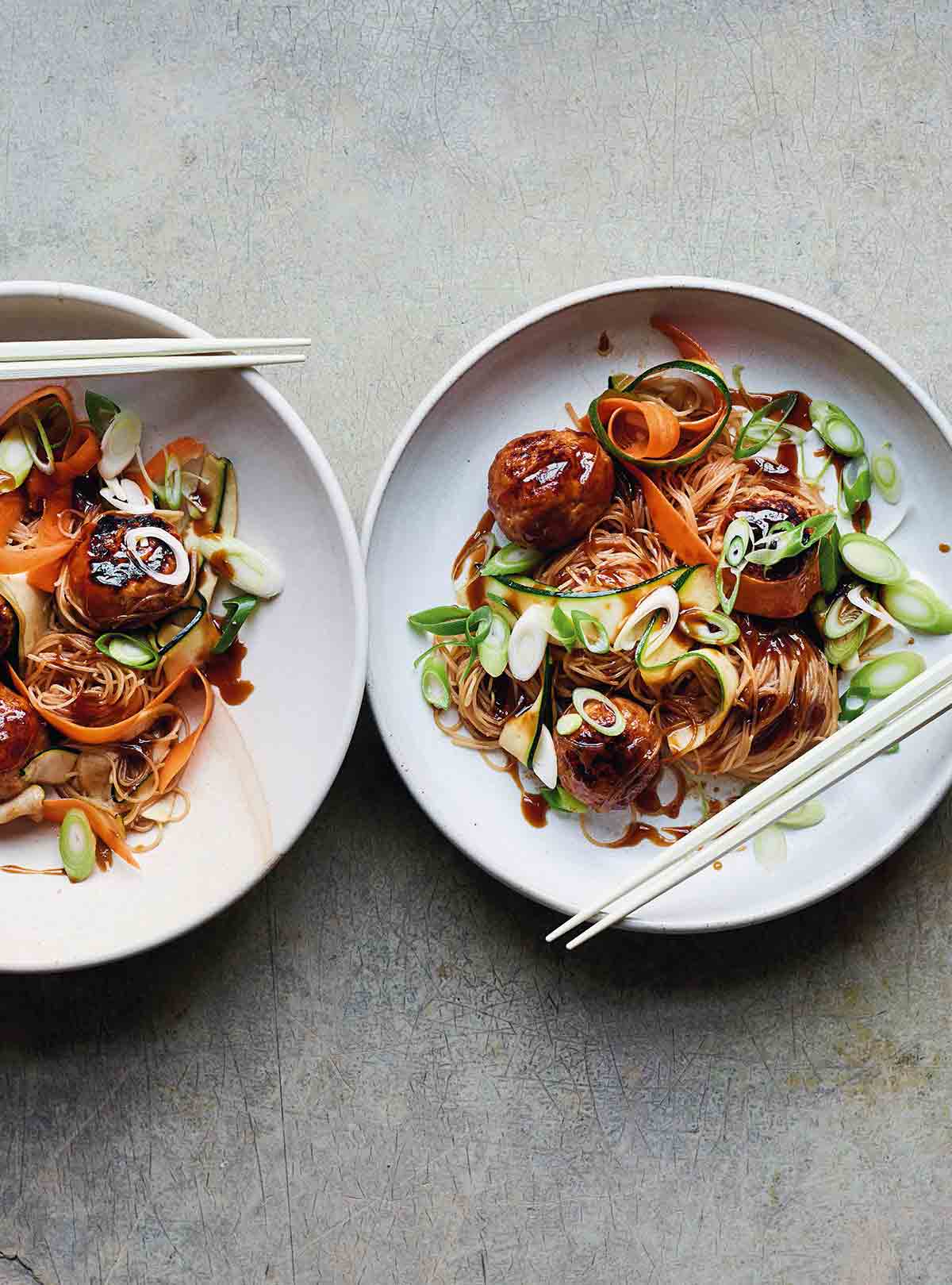 Two shallow bowls filled with turkey meatballs with rice noodle salad and a pair of chopsticks rests on the side of each bowl.