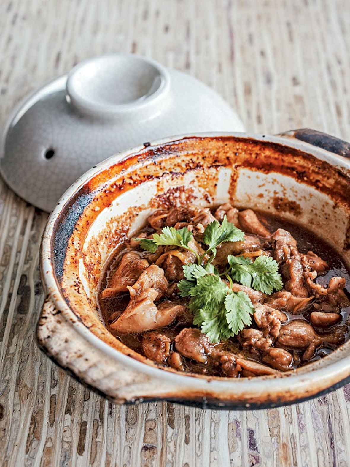 Clay pot filled with Vietnamese caramel chicken pieces and cilantro on a wooden table