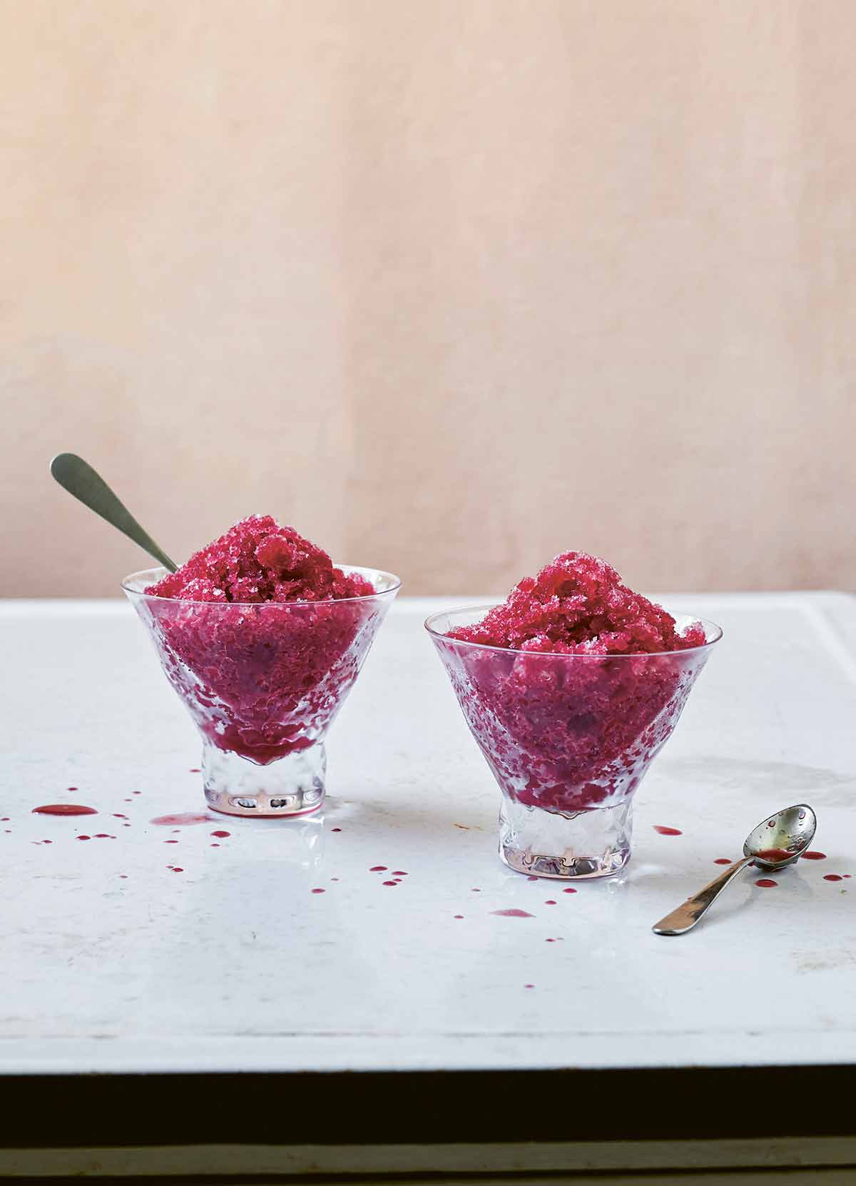 Two small glass dishes of blood orange granita, one with a spoon in it and the other with a spoon resting beside it.