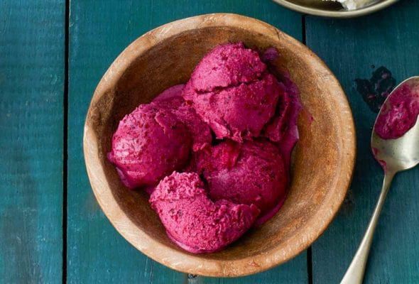 Four scoops of blueberry frozen yogurt in a wooden bowl with a spoon resting beside it.
