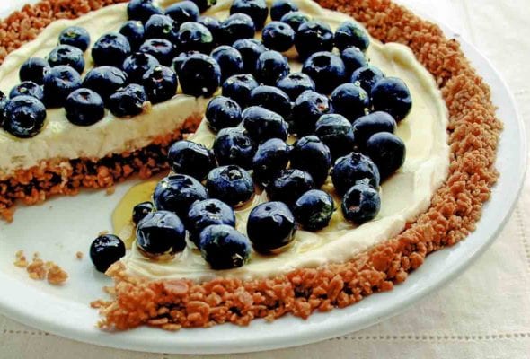 A blueberry pie with granola crust and blueberries on top with one slice missing.