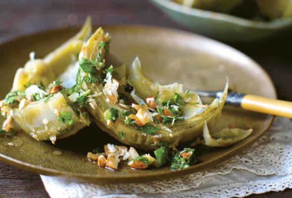 Braised artichokes on a plate, sprinkled with chopped almonds and parsley.
