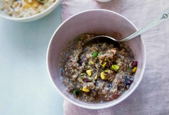 A white bowl half filled with breakfast quinoa, topped with chopped pistachios with a spoon resting in the bowl.