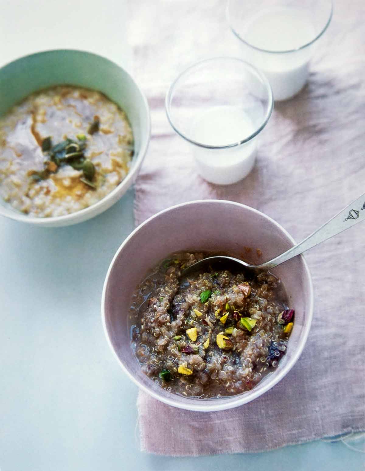 A white bowl half filled with breakfast quinoa, topped with chopped pistachios with a spoon resting in the bowl.