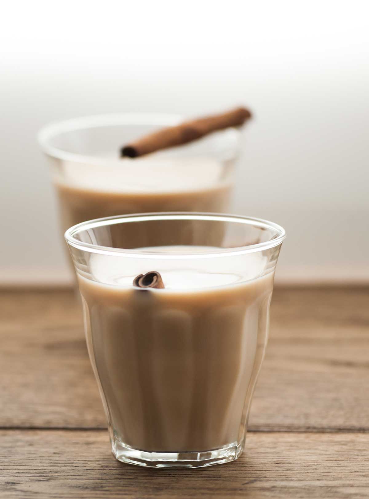 Two glasses of chai latte with cinnamon sticks on a wooden surface.