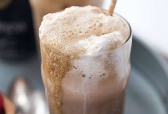 Two Guiness floats with straws on a grey metal try with a few spoons lying beside them.