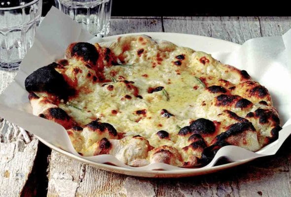 Jim Lahey's white pizza on a parchment-lined plate with water glasses stacked behind it.