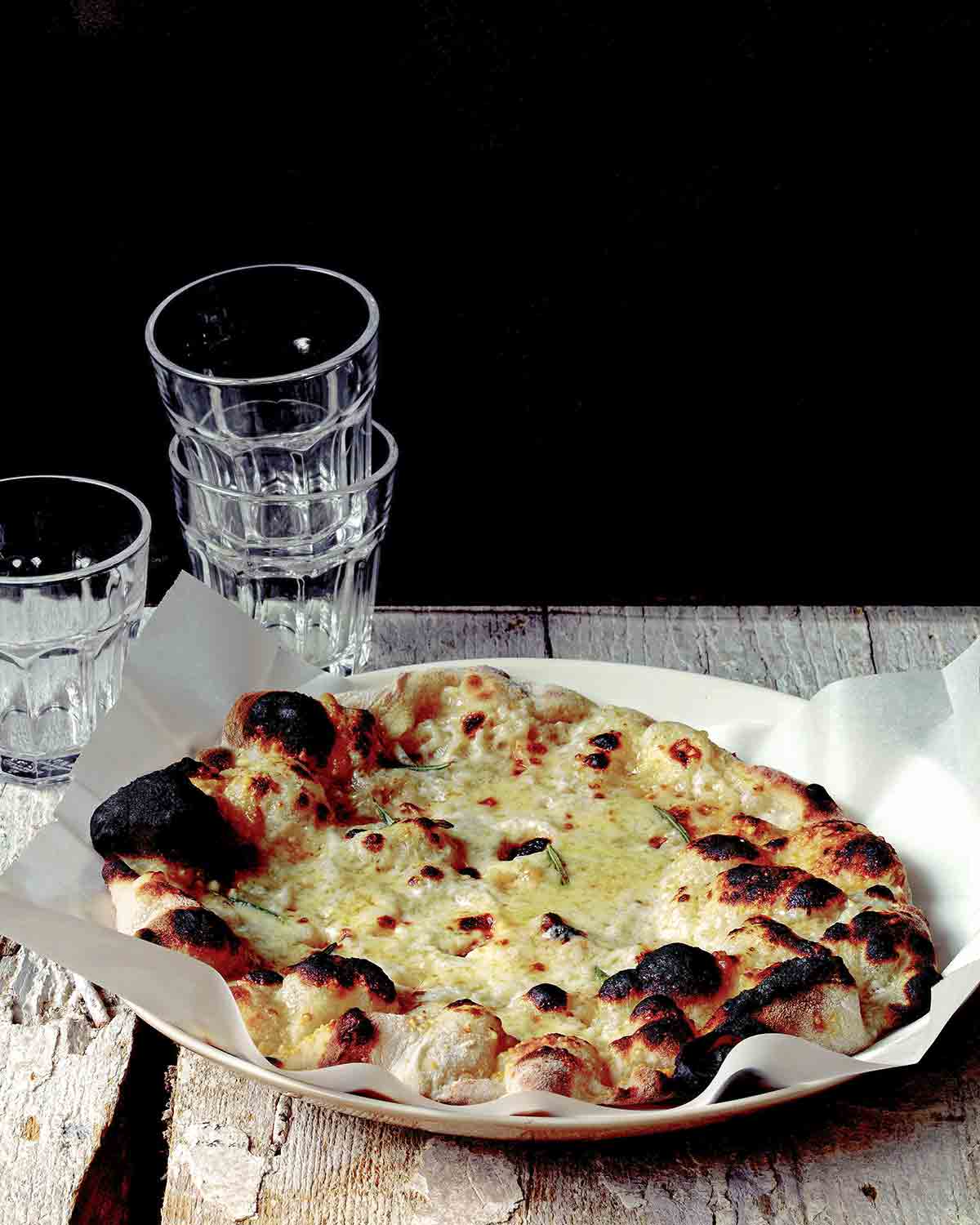 Jim Lahey's white pizza on a parchment-lined plate with water glasses stacked behind it.