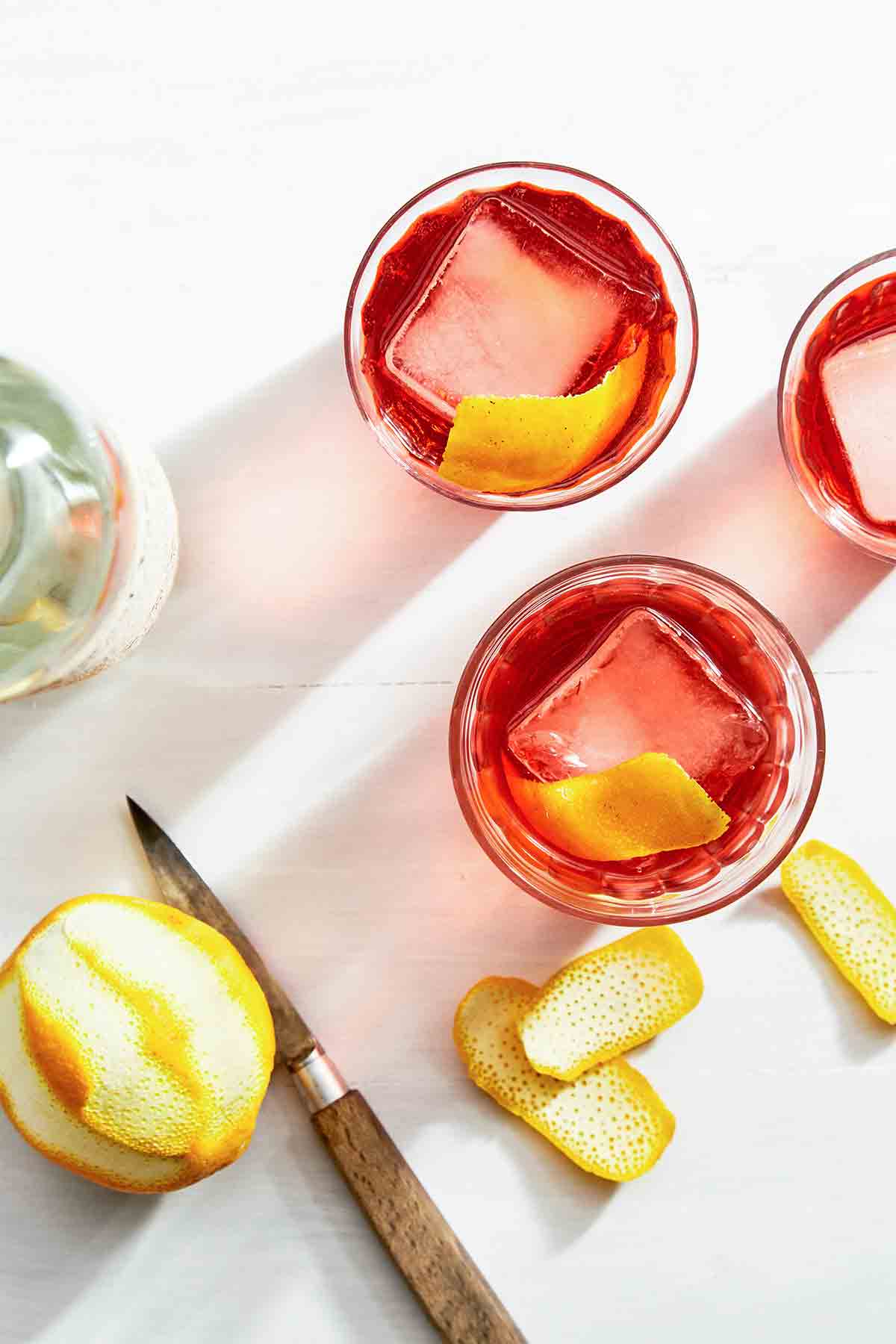 Three glasses of mezcal negroni garnished with orange peel.