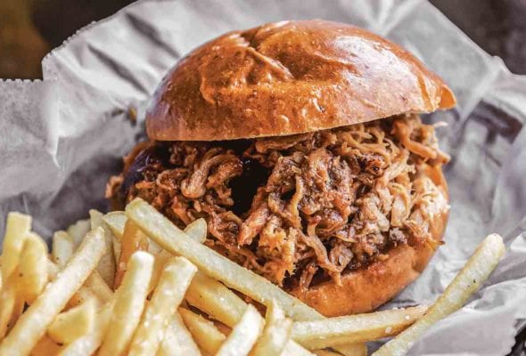 A smoked chicken sandwich and fries in a plastic basket lined with paper.