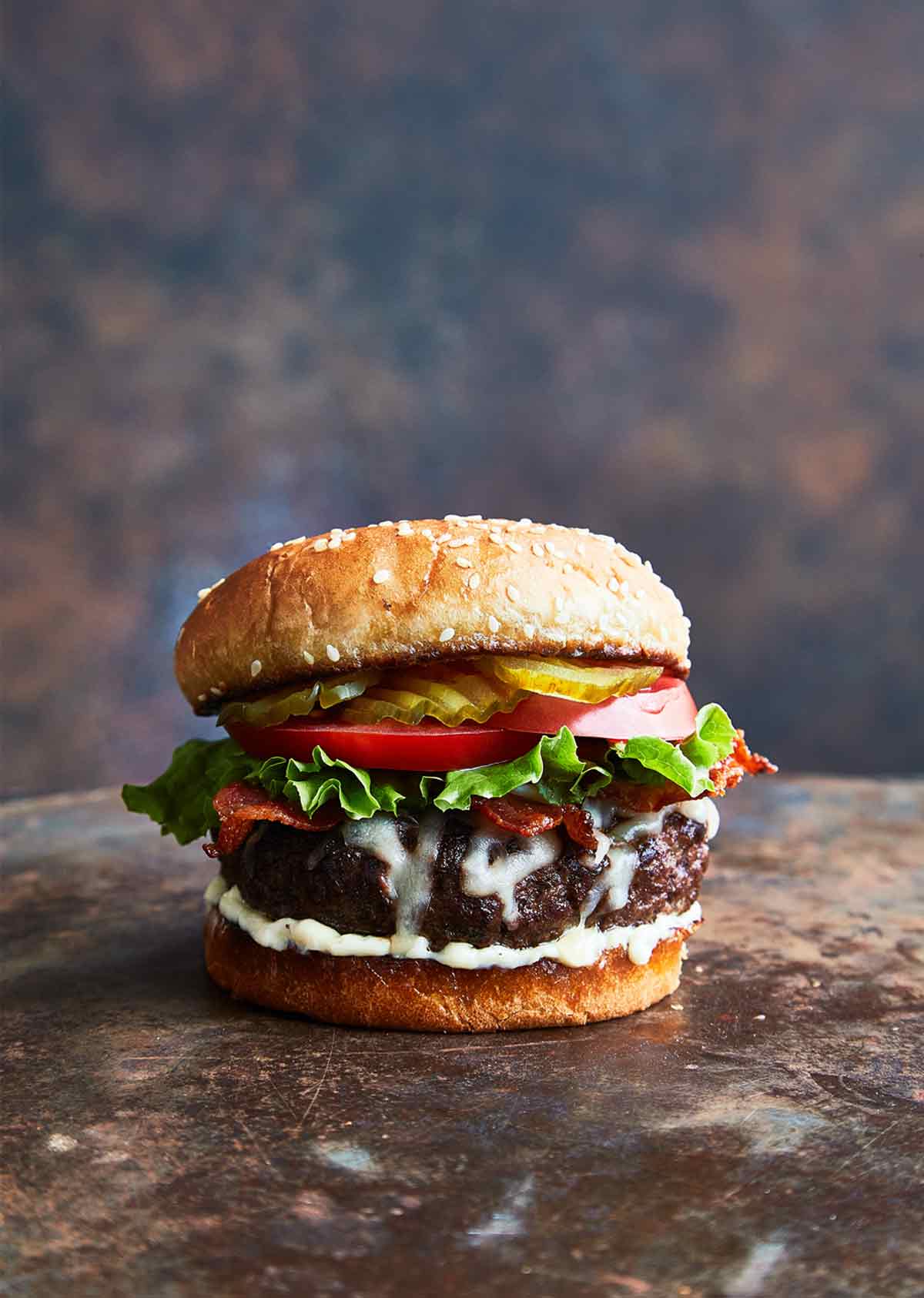 A bacon Swiss burger topped with lettuce, tomato, and dill pickle chips.