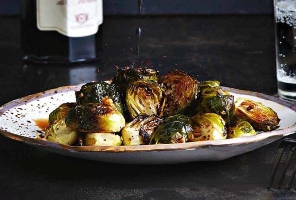 A plate of roasted Brussels sprouts with a drizzle of balsamic vinegar splashing down on it