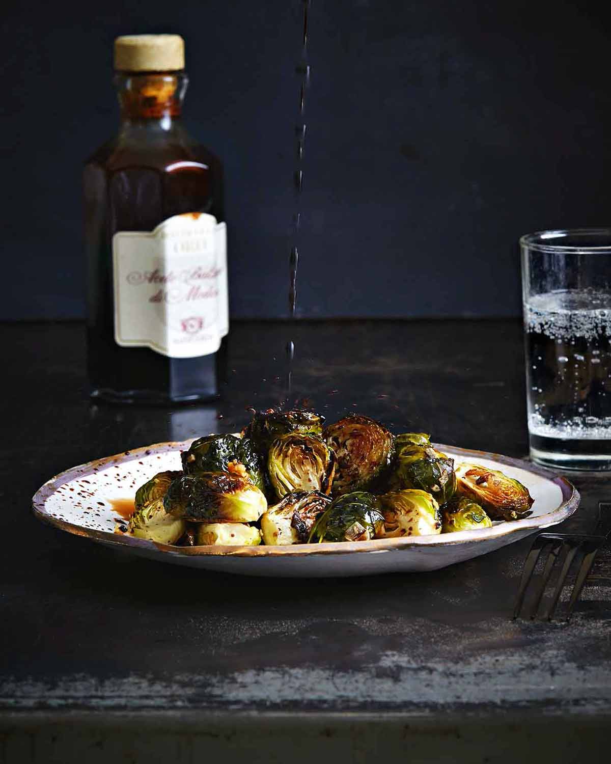 A plate of roasted Brussels sprouts with a drizzle of balsamic vinegar splashing down on it