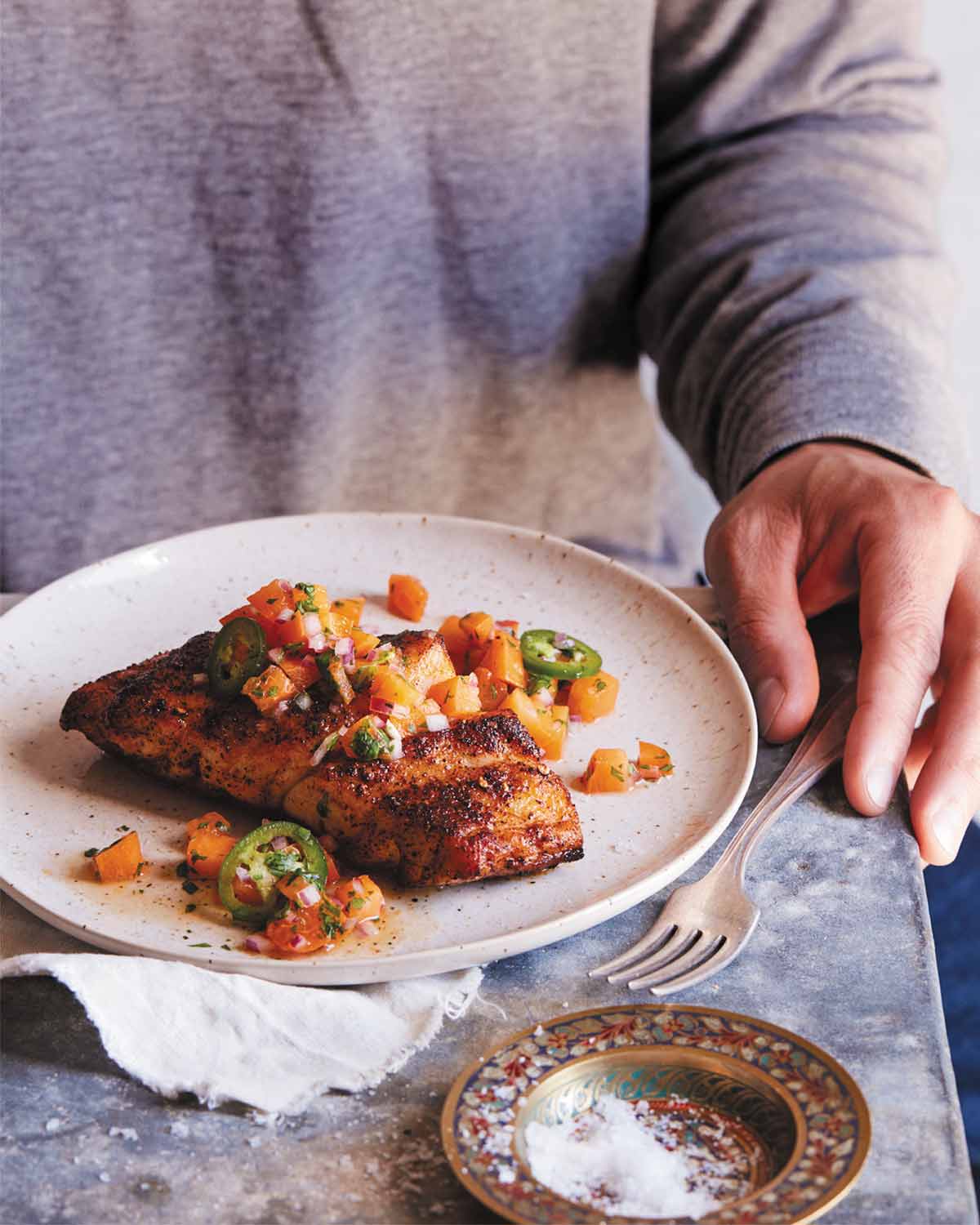 A person sitting in front of a plate of blackened grouper with peach jalapeño salsa.