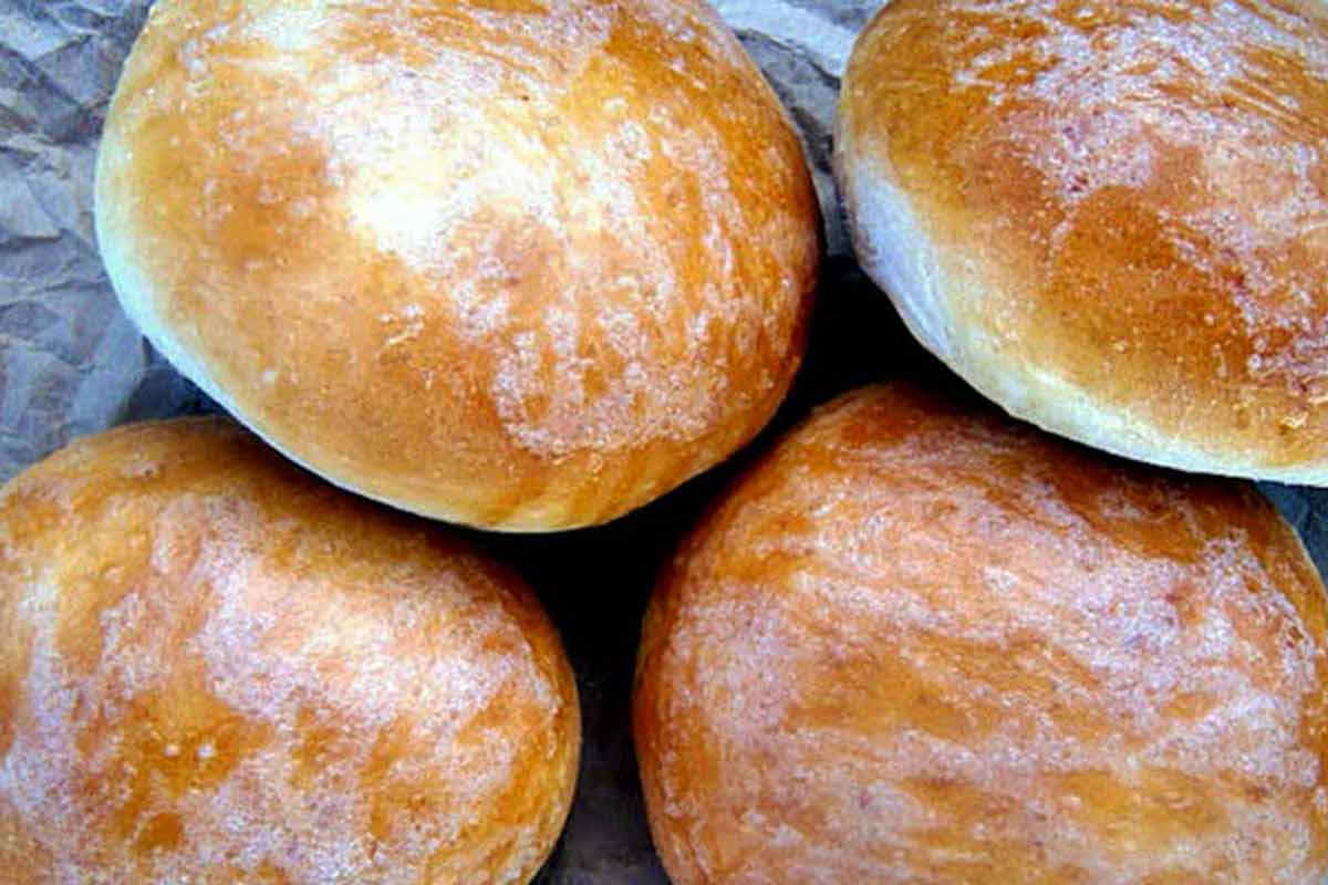 Four homemade burger buns dusted with flour on grey paper.