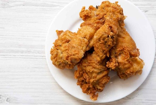 Three pieces of cornmeal crusted fried chicken on a white plate.
