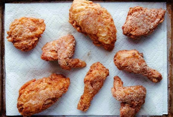 Seven pieces of gluten-free fried chicken on a paper towel-lined rimmed baking sheet.