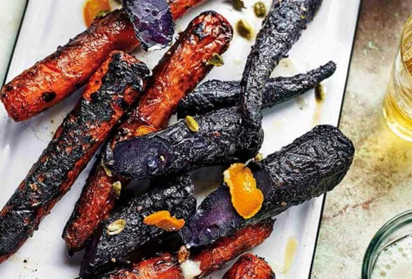 A white enamel platter topped with charred purple and orange grilled carrots.