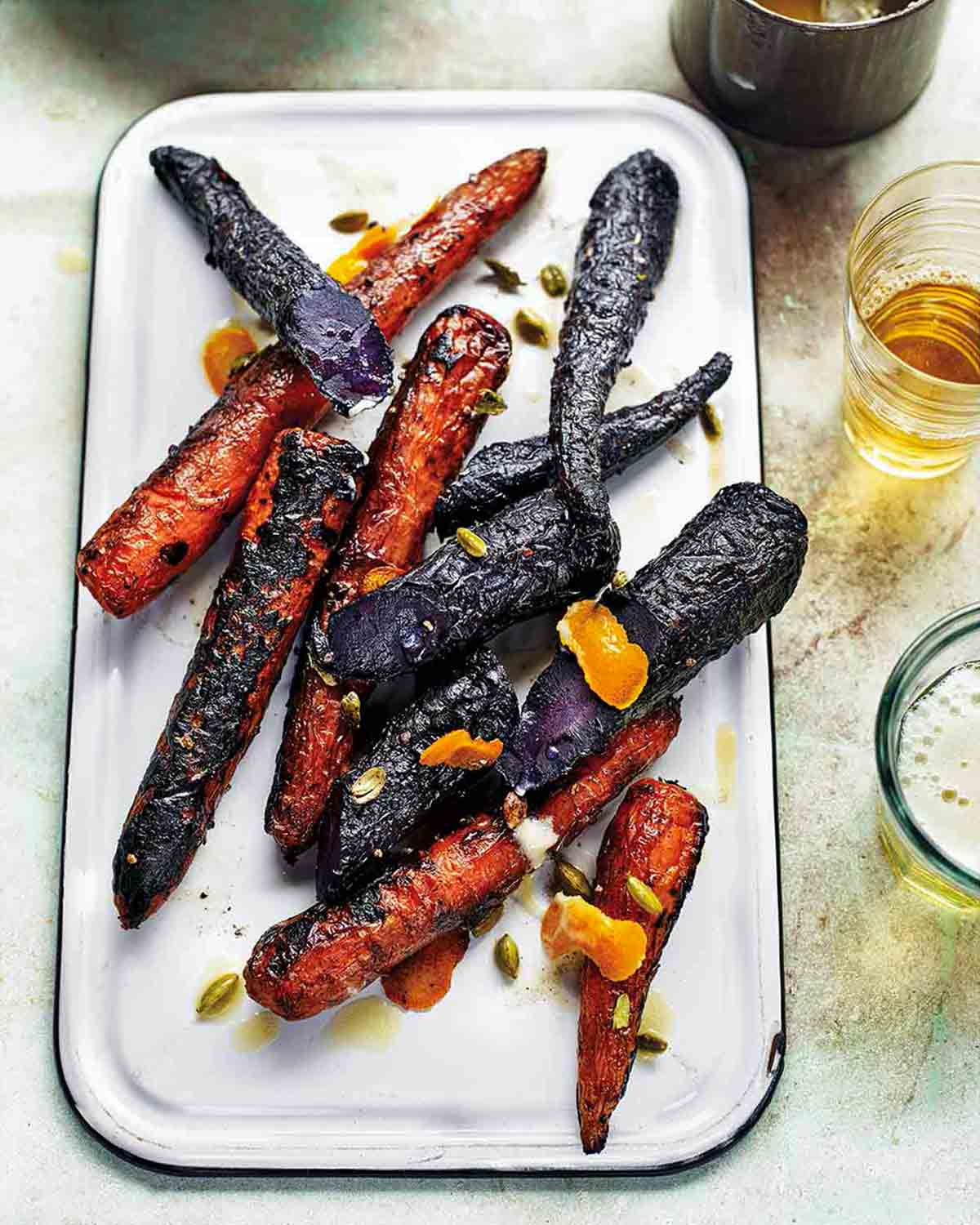 A white enamel platter topped with charred purple and orange grilled carrots.