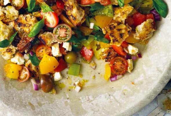 A large bowl filled with grilled panzanella, with cherry tomatoes, torn bread, and basil leaves.