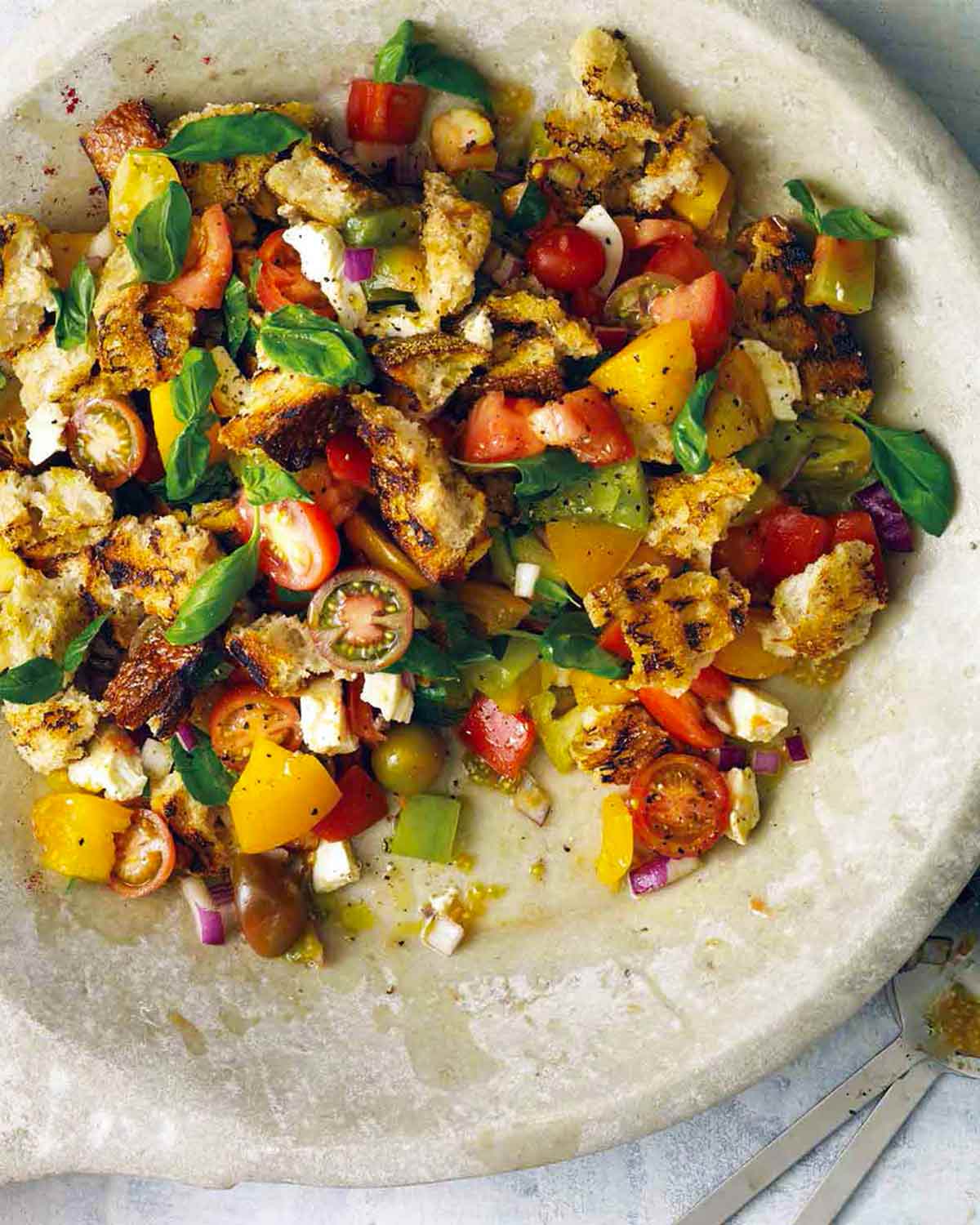 A large bowl filled with grilled panzanella, with cherry tomatoes, torn bread, and basil leaves.