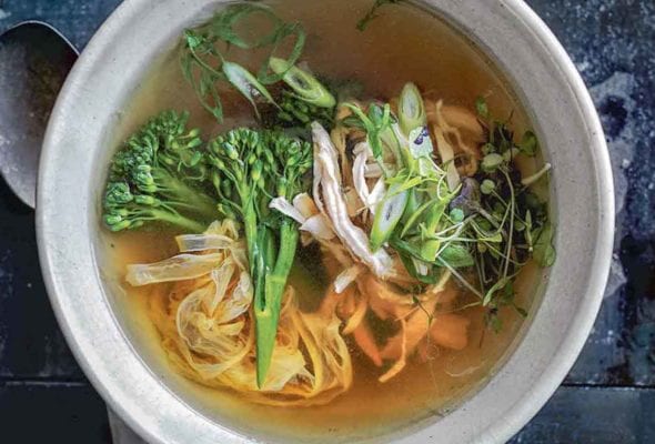 A bowl of healthy egg drop soup with shredded chicken, green onions, broccoli rabe, noodles, and sprouts