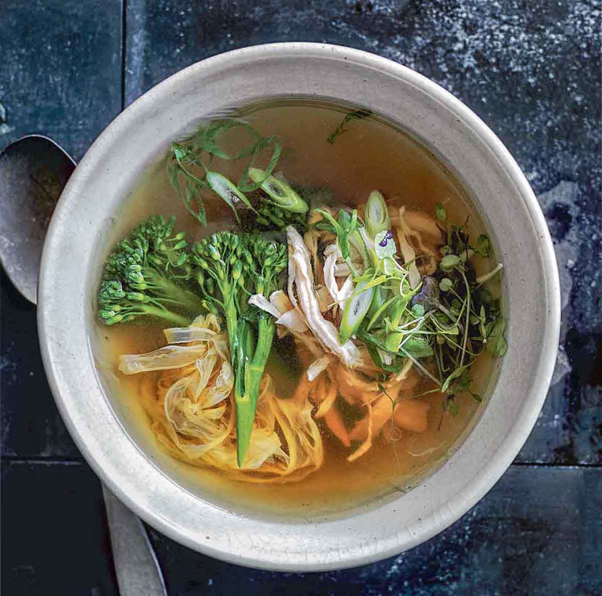A bowl of healthy egg drop soup with shredded chicken, green onions, broccoli rabe, noodles, and sprouts