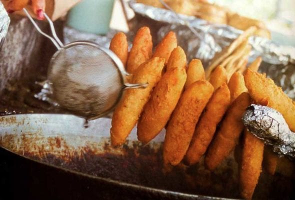 Jamaican fried dough on a skewer over a large pot of oil.