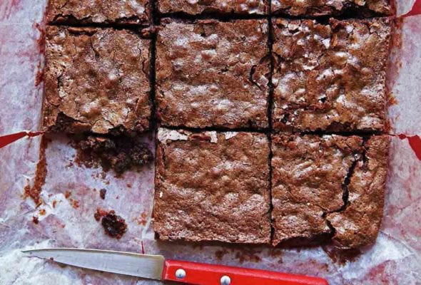 A slab of Katharine Hepburn brownies cut into 9 pieces, on parchment paper, with a knife nearby