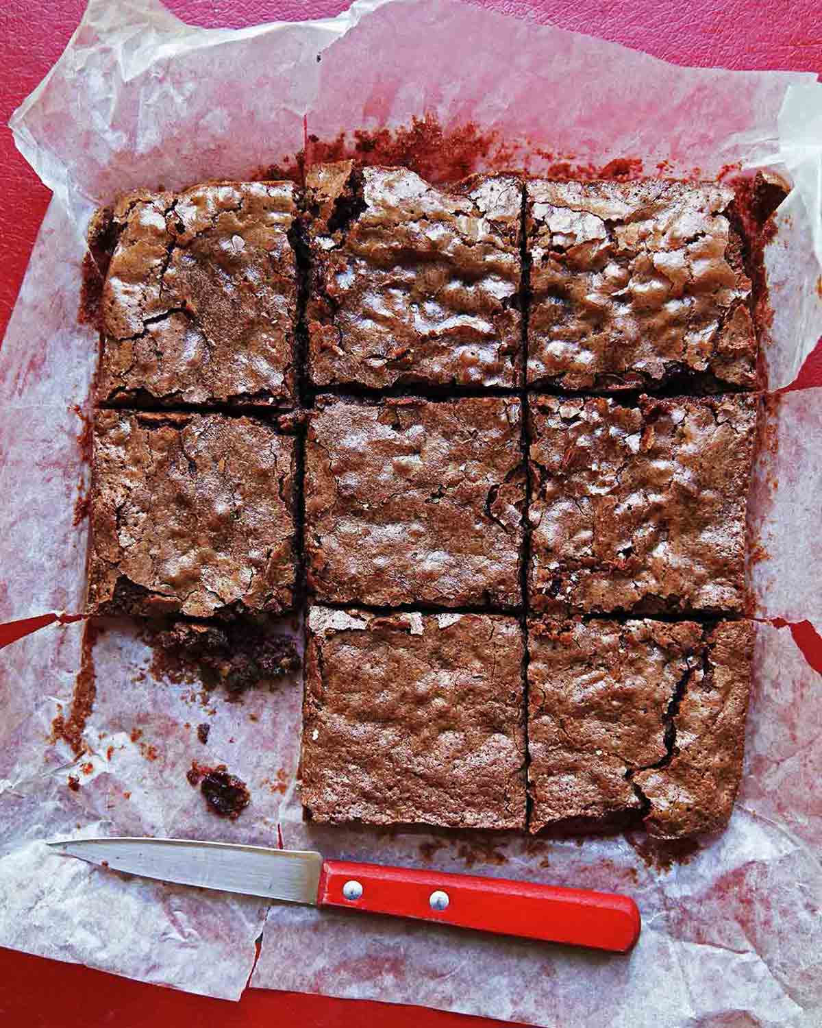 A slab of Katharine Hepburn brownies cut into 9 pieces, on parchment paper, with a knife nearby