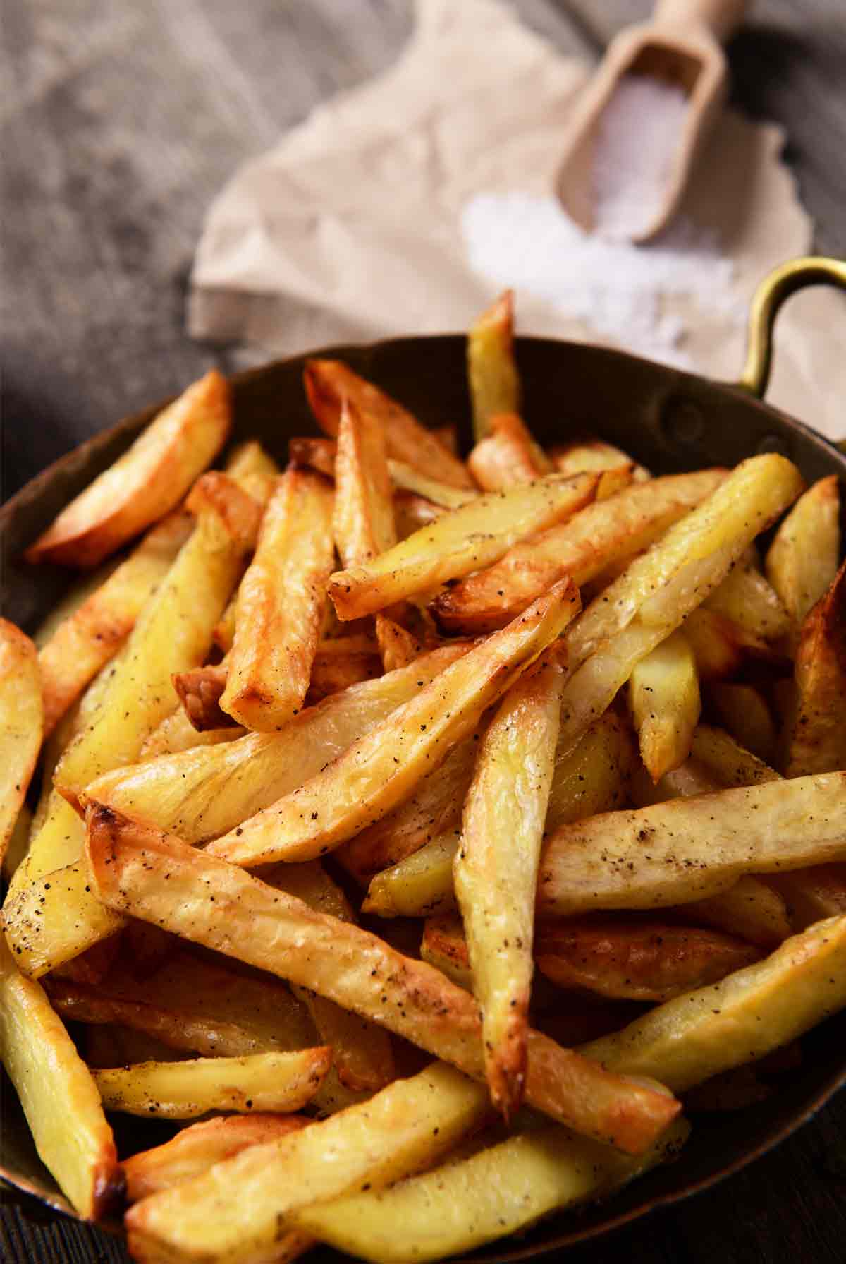 A metal bowl with handles filled with seasoned perfect French fries.