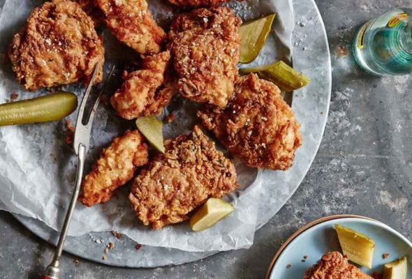 A platter of pickle-brined fried chicken with pieces of dill pickle, and a bottle of beer.