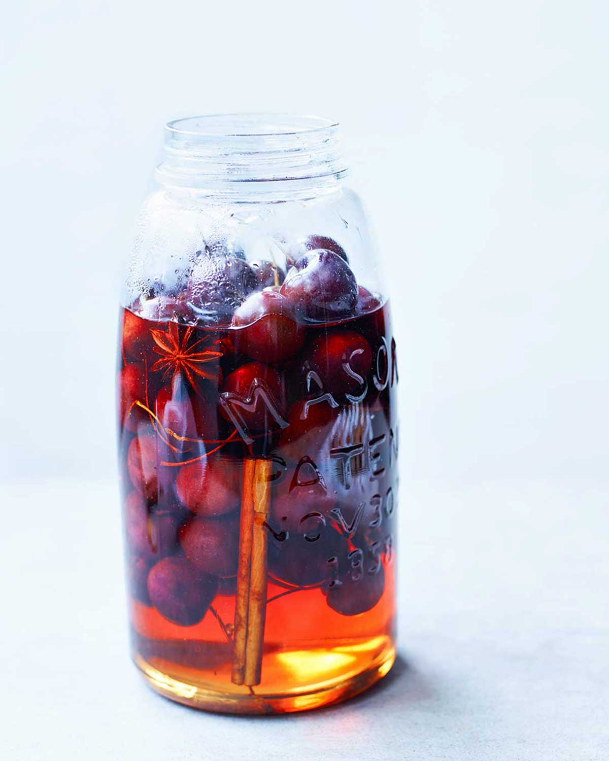 A mason jar mostly filled with pickled cherries, pickling liquid, star anise, and a cinnamon stick.