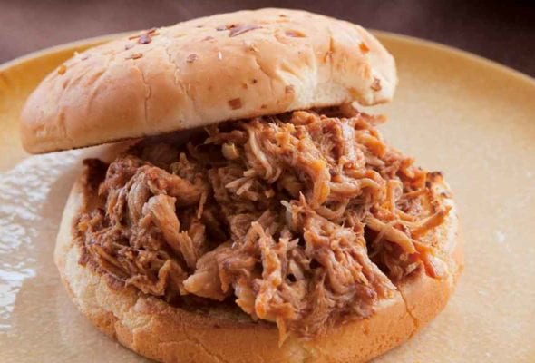 Slow cooker pulled pork piled on a bun on a plate.