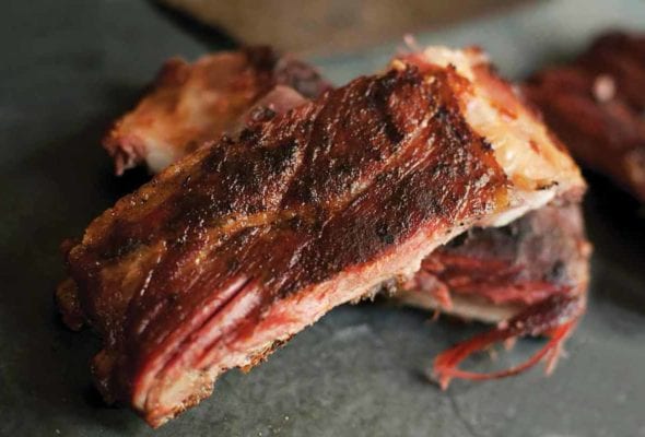 Two smoked spareribs and a knife on a slab of stone