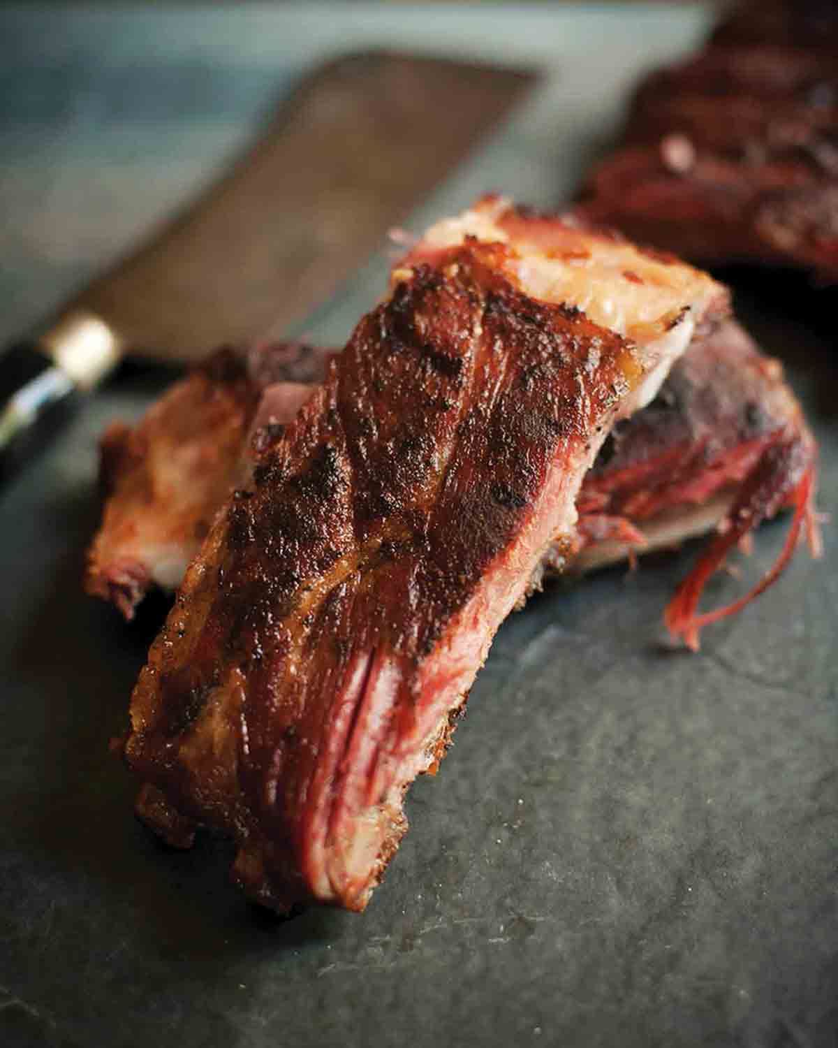 Two smoked spareribs and a knife on a slab of stone