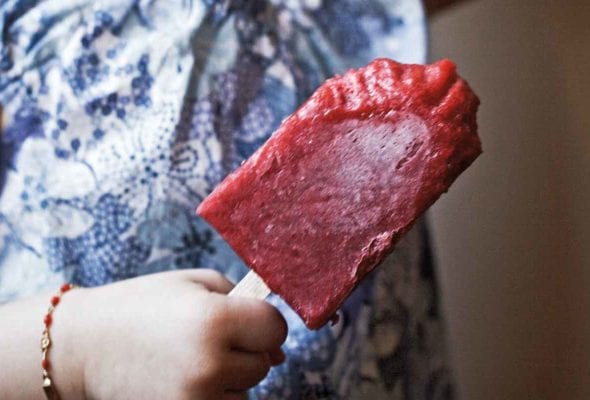 A little girl eating a strawberry ice pop.