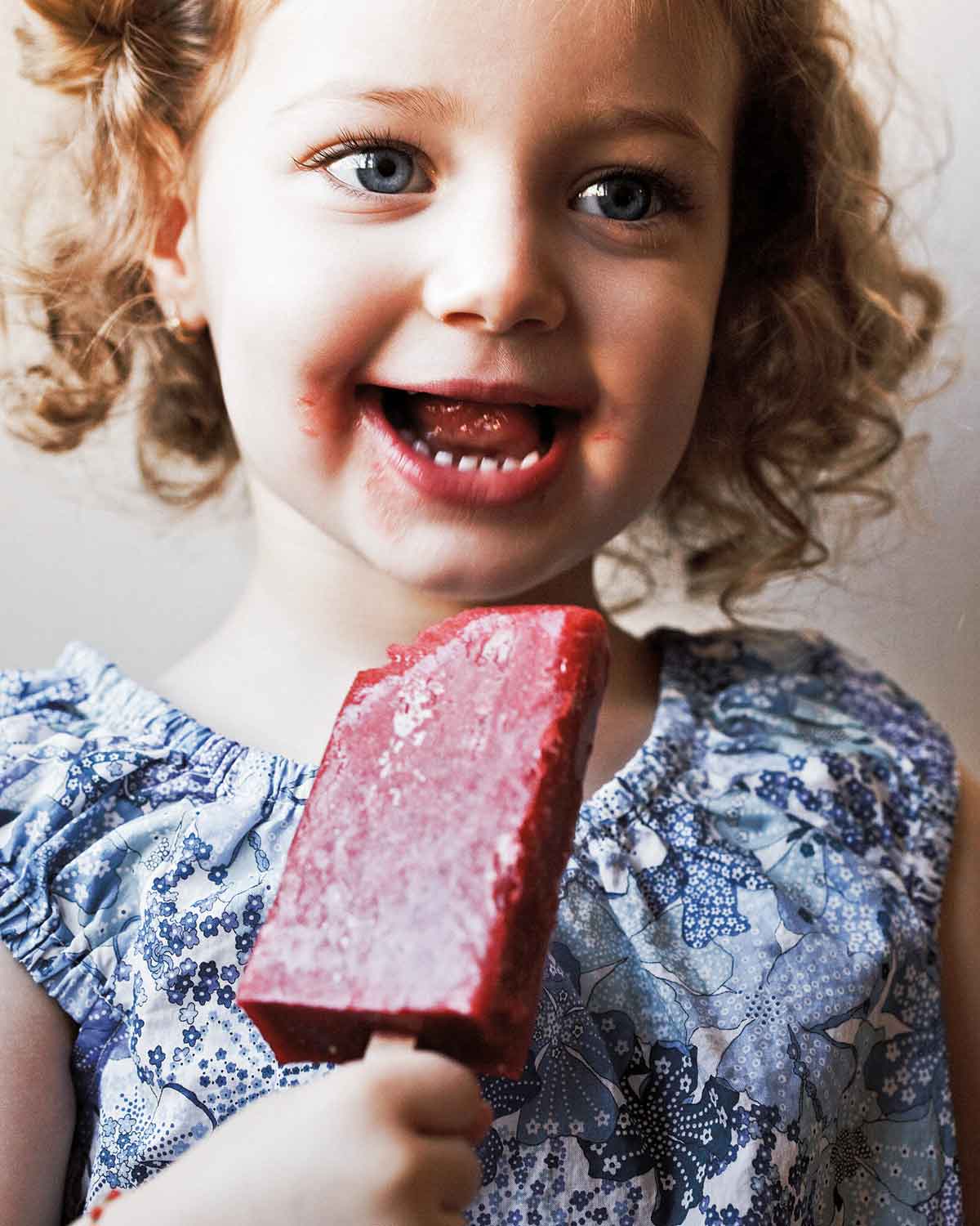 A little girl eating a strawberry ice pop.