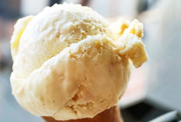 A person holding an ice cream cone filled with rich vanilla ice cream.