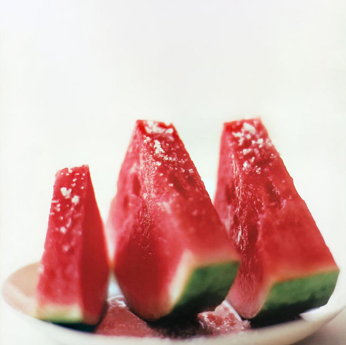 Three slices of watermelon with fleur de sel sprinkled over top.