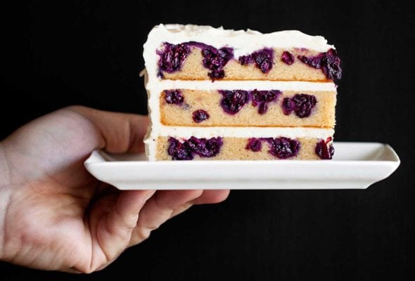 A white plate with a slice of blueberry-lemon layer cake