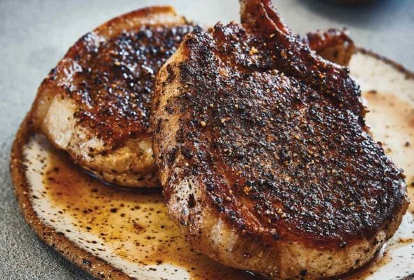 Two bone-in grilled Cambodian pork chops on a plate.