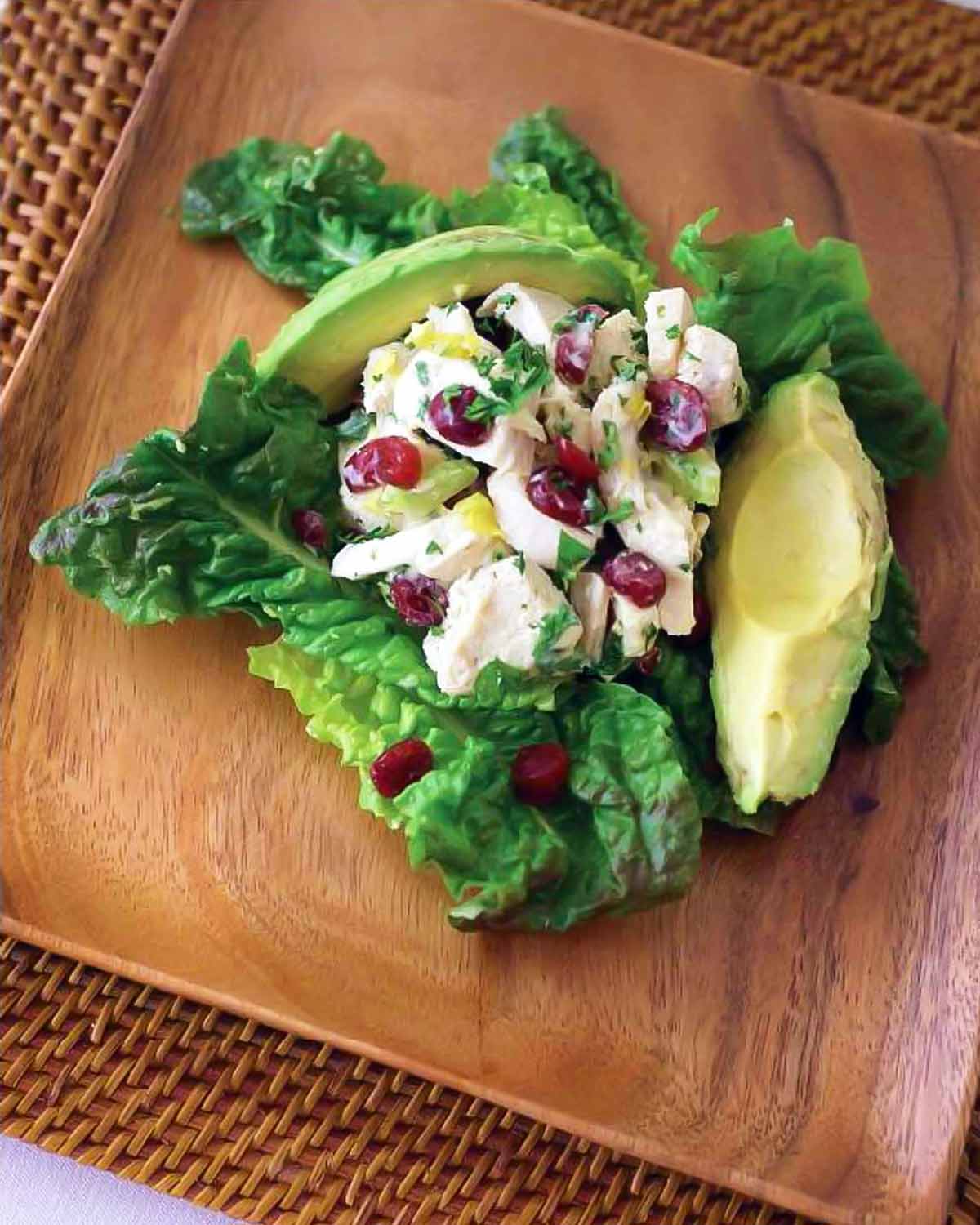 A serving of chicken avocado cranberry salad on a square wooden plate.