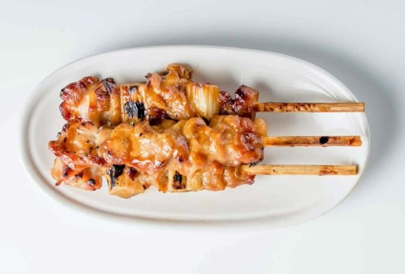 A white oval serving platter topped with three skewers of chicken yakitori with honey sauce.