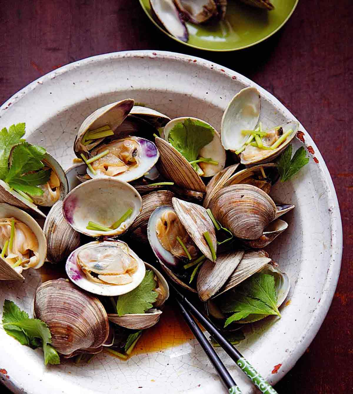 Bowl of grilled littleneck clams with soy sauce, cilantro leaves, and chopsticks
